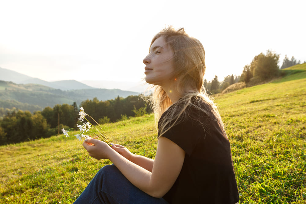 Beautiful blonde girl enjoying mountains view, holding camomiles.